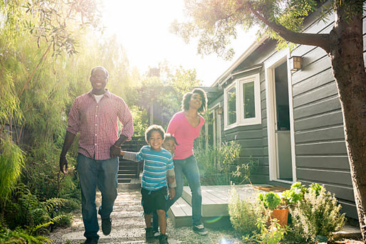 A happy family enjoys a sunny day walking alongside their home.