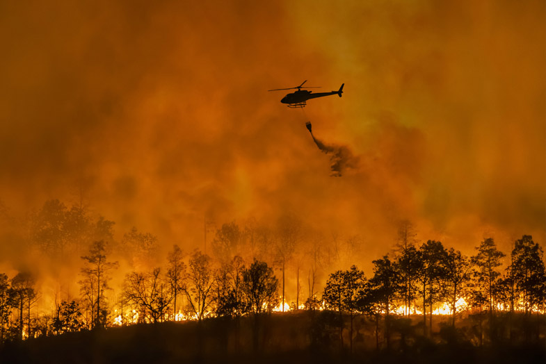 Helicopter flies over brush fire